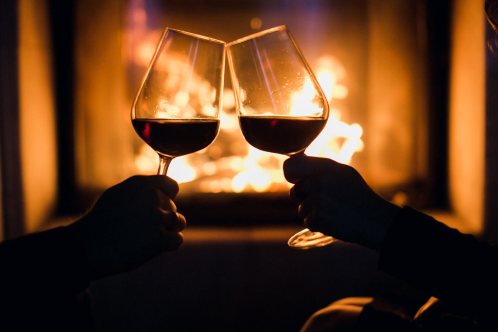 couple with two glasses of red wine in front of a fireplace