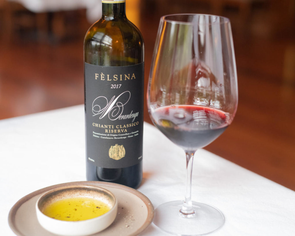 Bottle of wine with a glass partially full and a dish of olive oil